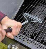 A man using a two-handed grip on the barbecue brush handle to clean a grill