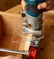 A woodworker uses a cabinet hinge template to guide a compact router when cutting a hinge mortise