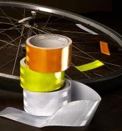 Three rolls of reflective tape piled next to a bicycle wheel with reflective tape attached to the spokes