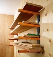 Various sizes of wooden boards stacked on a Bora four-shelf lumber rack mounted on a plywood wall