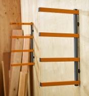 A Bora four-shelf lumber rack mounted on a plywood wall, near loose boards ready to be stacked