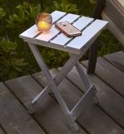 Candle and phone sitting on an unfolded side table on a deck