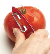 Personne pelant une tomate avec un éplucheur à lame dentelée