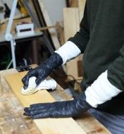 A woodworker wearing glove liners under nitrile gloves while staining a board