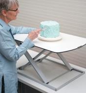 A woman frosts a cake on the Height-Adjustable Work Stand