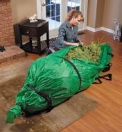 Femme refermant un sac de transport pour sapin de Noël autour d'un sapin reposant au sol