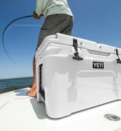 A Yeti cooler sits on boat deck with a man fishing in the background