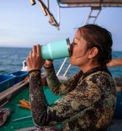 Une femme buvant une boisson dans un gobelet Yeti de couleur écume de mer à bord d'un bateau