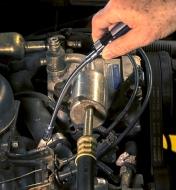 A person uses the flex-shaft nut driver to tighten a hose clamp in a truck’s engine compartment