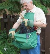 A man wearing the kangaroo pocket apron collects garden waste in the pocket