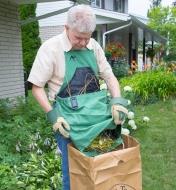 A man wearing the kangaroo pocket apron dumps garden waste from the pocket into a paper bag