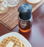 Dripless Bottle filled with syrup, sitting on a table next to a plate of waffles