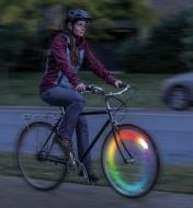A woman rides a bicycle at night with a SpokeLit wheel light installed in color-changing mode 
