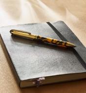 Example of a Surfix Duo gold/gunmetal pen turned from an acrylic acetate blank, lying on a closed notebook