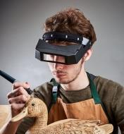 Homme portant une loupe binoculaire tout en pyrogravant un canard en bois