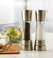 A set of Cole & Mason salt and pepper mills standing on a marble countertop next to a bowl of salad
