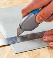 Safety utility knife cutting linoleum along the edge of a steel ruler
