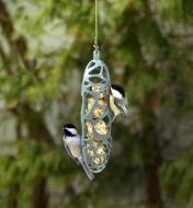 Two chickadees feed from the suet bird feeder hanging in a yard