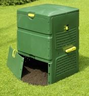 Composter in a garden with the bottom compartment open, releasing finished compost
