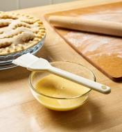 The pastry brush rests on a bowl of egg wash before painting on pie crust
