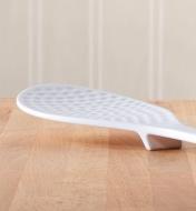 Rice paddle on a wooden counter, with a small foot on the underside raising the end off the countertop