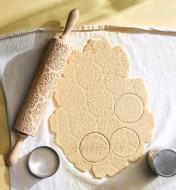 Rouleau à gaufrer sur un linge à pâtisserie avec une abaisse de pâte gaufrée et découpée par un emporte-pièce rond