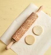 Kaleidoscope patterned rolling pin beside two embossed cookies, comparing before and after baking