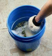 In a water-filled pail, a wash mitt is rubbed against the wash pail insert to loosen trapped grit