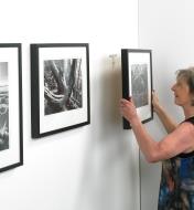 A woman hanging a row of pictures on adjustable picture hangers