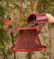 Seeds poured into collapsible bird feeder through an opening in the top