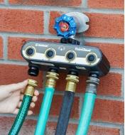Four garden hoses attached to a Wi-Fi Water Timer mounted on an outdoor faucet 