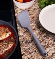 Right-Hand Silicone Flipper resting between a plate on a counter and a pan of food on a stovetop