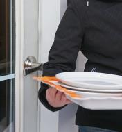 A woman carrying a tray of dishes opens a door with the push of her elbow on the handle 