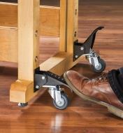 A foot depresses the pedal of a workbench caster, lowering it into position to contact the floor