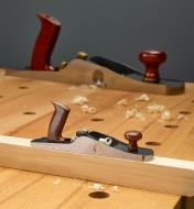 The miniature bevel-up jack plane sits on a workpiece with a full-size low-angle jack plane shown in the background
