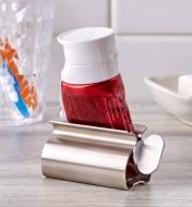 The tube squeezer holding a rolled-up tube sits on a bathroom counter