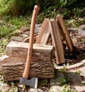 Small forest axe leaning against a stack of logs next to a fire pit