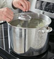 Lowering the Large Infuser Basket into a large pot of liquid on a stove