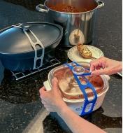 Attache en silicone mise en place pour retenir le couvercle d'un plat de cuisson et, en arrière-plan, une casserole fermée avec une autre attache