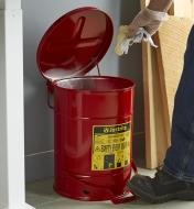 Personne jetant un chiffon imbibé d'huile dans une poubelle de sécurité pour déchets inflammables dans un atelier