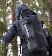 A rain-splashed hiker wears a waterproof dry bag backpack that has a drink bottle in the mesh side pocket