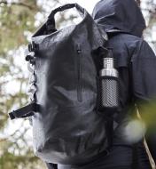 Vue de côté du sac à dos étanche montrant une poche à fermeture à glissière remontée et une poche en filet qui contient une bouteille