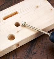 Multi-angle drill bit resting on a wood block with examples of holes and grooves made by the bit