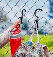 Two Heroclip carabiners used to hang a child’s water bottle and backpack on a schoolyard fence