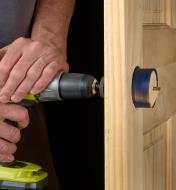 Using a carbide-tipped hole saw to drill through a wooden door, creating a bore hole for a doorknob