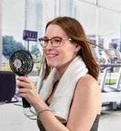 A woman uses a rechargeable portable turbo fan to cool off while working out at a gym