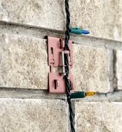 Brick clamp supporting a string of Christmas lights vertically on a brick wall