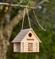 An assembled log cabin birdhouse hangs from a tree