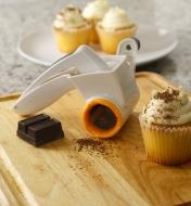 The rotary cheese grater next to cupcakes topped with grated chocolate