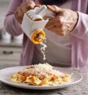 Using the rotary cheese grater to grate cheese over a dish of pasta